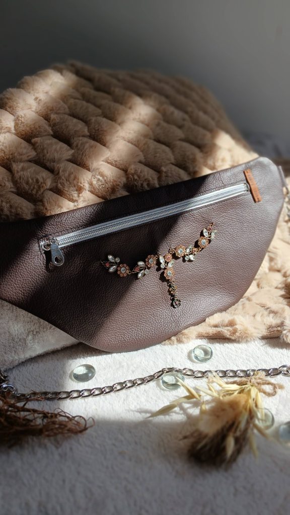Vue de face du sac banane Floraline, en cuir surcyclé marron. Avec son collier de seconde main aux motifs floraux et ses strass scintillants, il est un accessoire élégant, féminin et singulier, fait main.