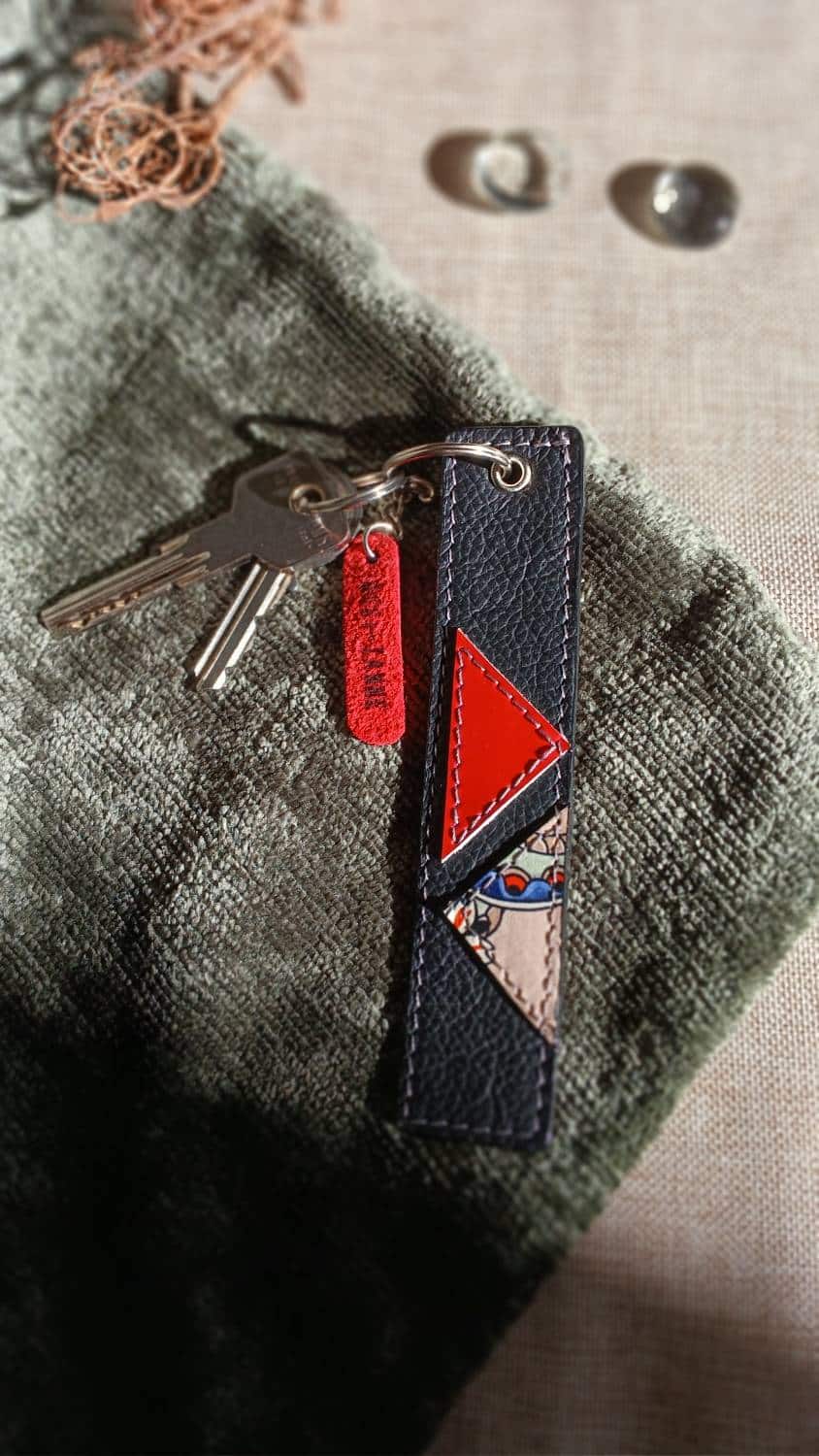 Vue avant du porte-clés Coq'Uette en cuir surcyclé rouge et noir. Il reprend une chute de cuir à motif coq et un cuir rouge ciré. Il fait partie de la catégorie les Complices « Coq'Uette ». C'est un accessoire féminin, unique, affirmé, fait main.