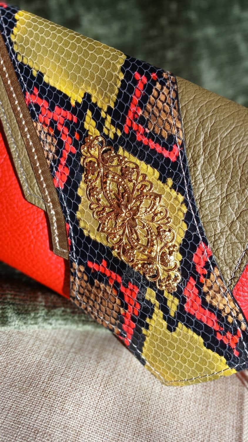 Vue zoomée sur le bijou de seconde main du sac Serpentine. Une ancienne broche cousue main sur le cuir surcyclé effet serpent. C'est un accessoire féminin, élégant, affirmé, fait main.