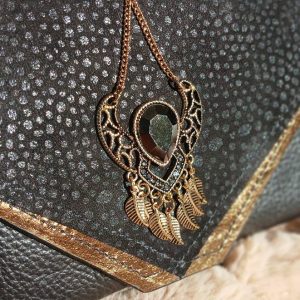 Vue sur le bijou du sac Galante, de la catégorie Les Complices Galante, en cuir upcyclé noir et bronze, fait main. Avec ses tons subtiles et son bijou de seconde main assorti, féminité assumée. Une création artisanale et unique.